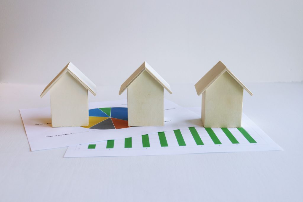 Three miniature wooden house models set on top of financial growth charts, representing smart real estate investing strategies.