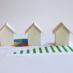 Three miniature wooden house models set on top of financial growth charts, representing smart real estate investing strategies.